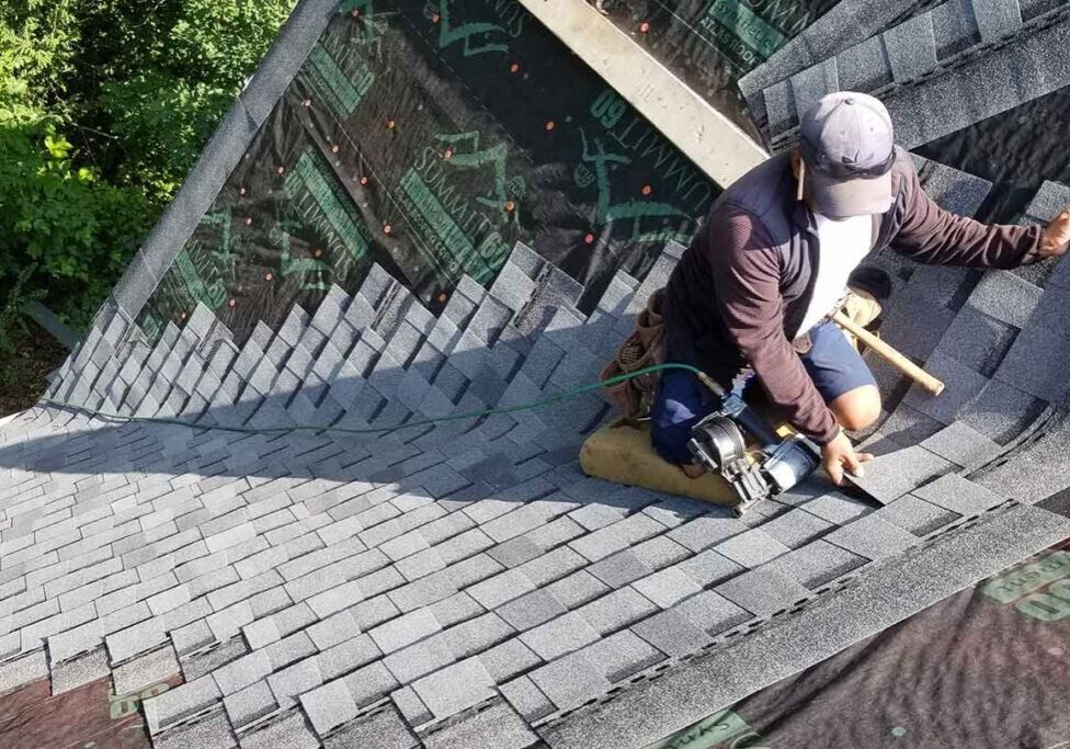 Worker installing shingles on a roof under sunny weather.
