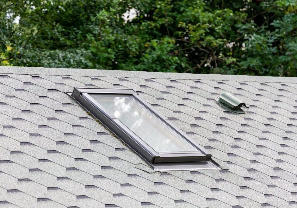 A roof with gray shingles and a rectangular skylight window.